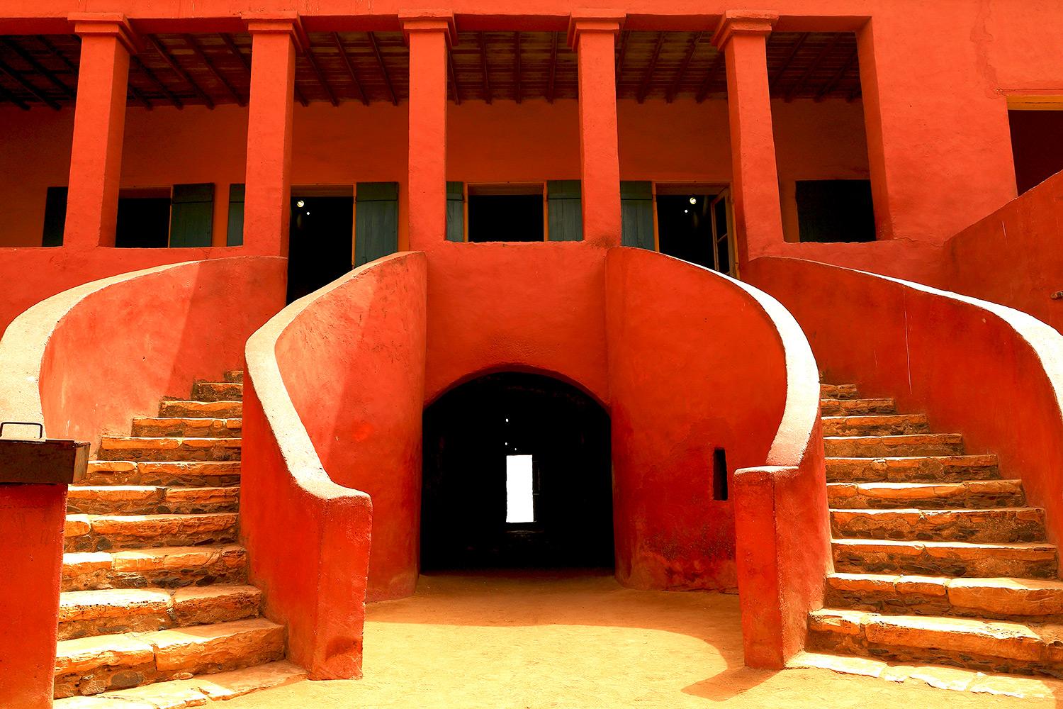 Red building with two staircases, a door in the middle, and pillars above